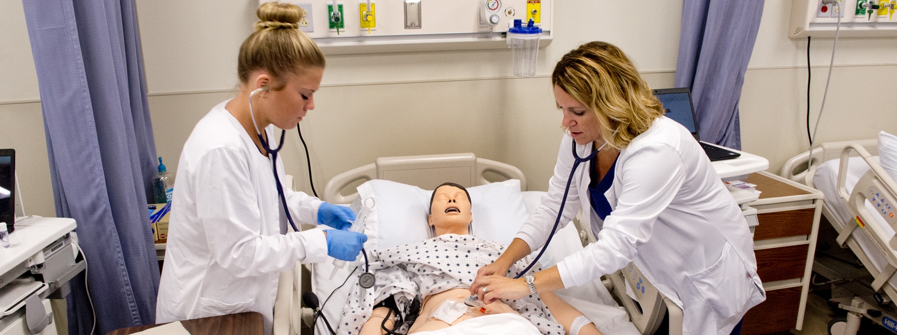 Two students in a nursing lab practicing skills on a practice dummy