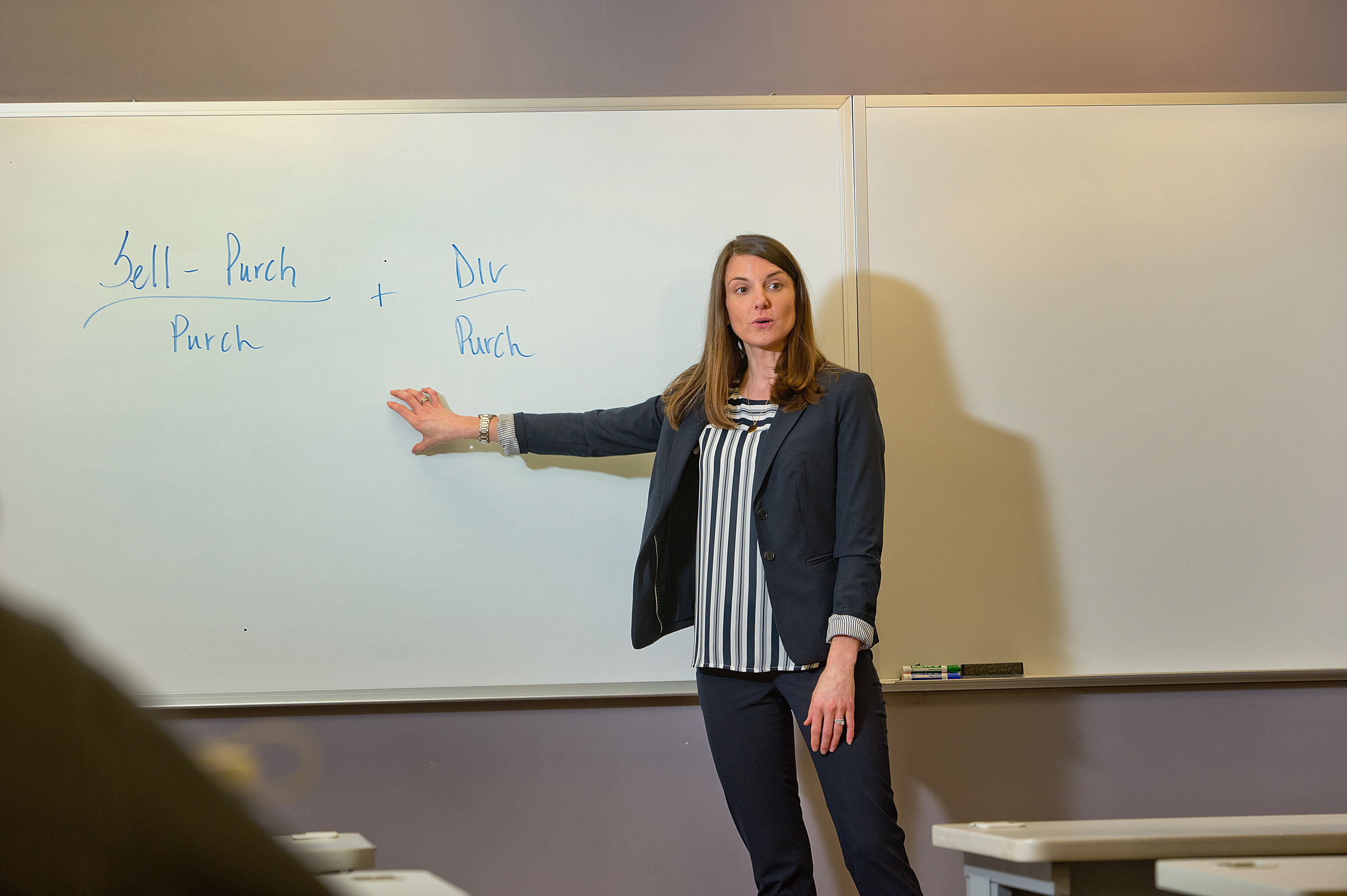 Professor teaching a class while pointing at a whiteboard 