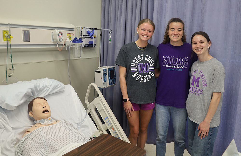 Three Mount Union students posing next to simulation dummy