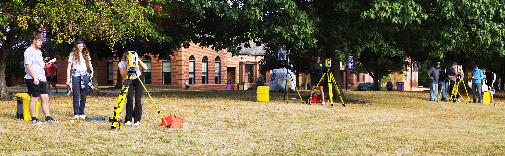 students using surveying equipment in campus quad