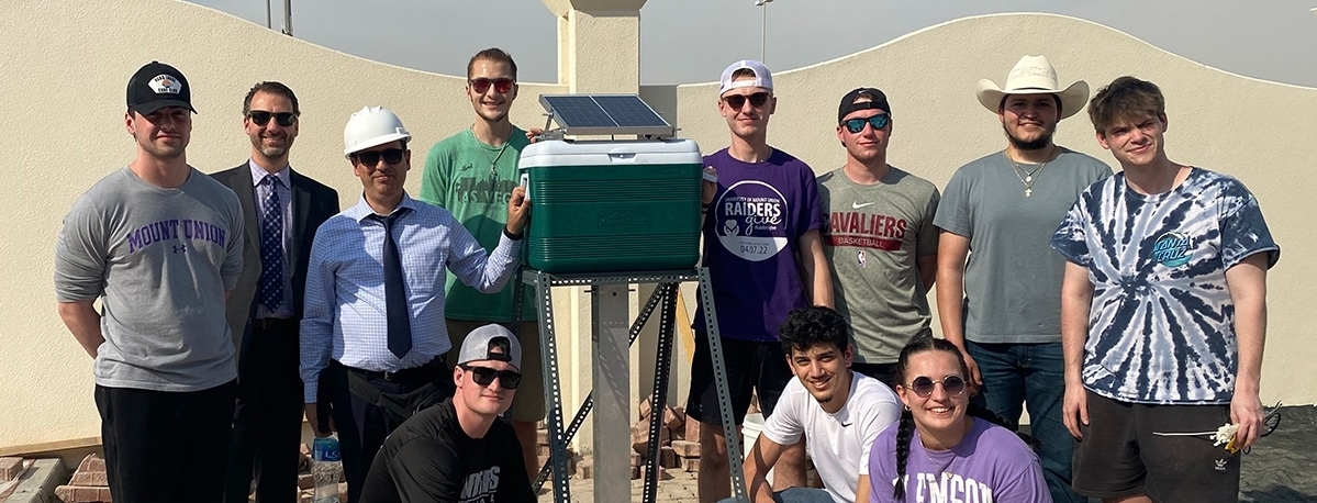 faculty and students standing beside project