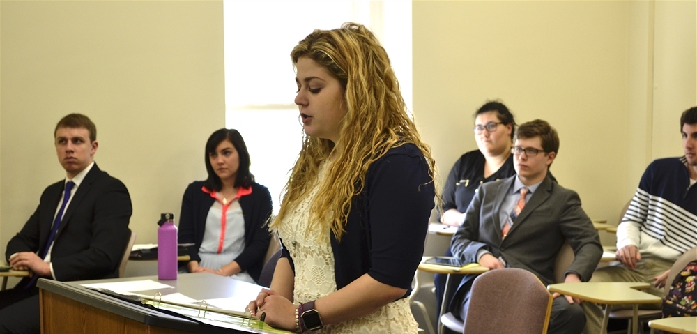 Student standing at a podium presenting to class