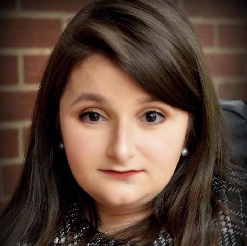 Addie has dark hair and is in front of a brick background.
