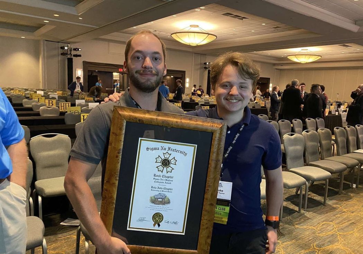 two students standing with fraternity award plaque
