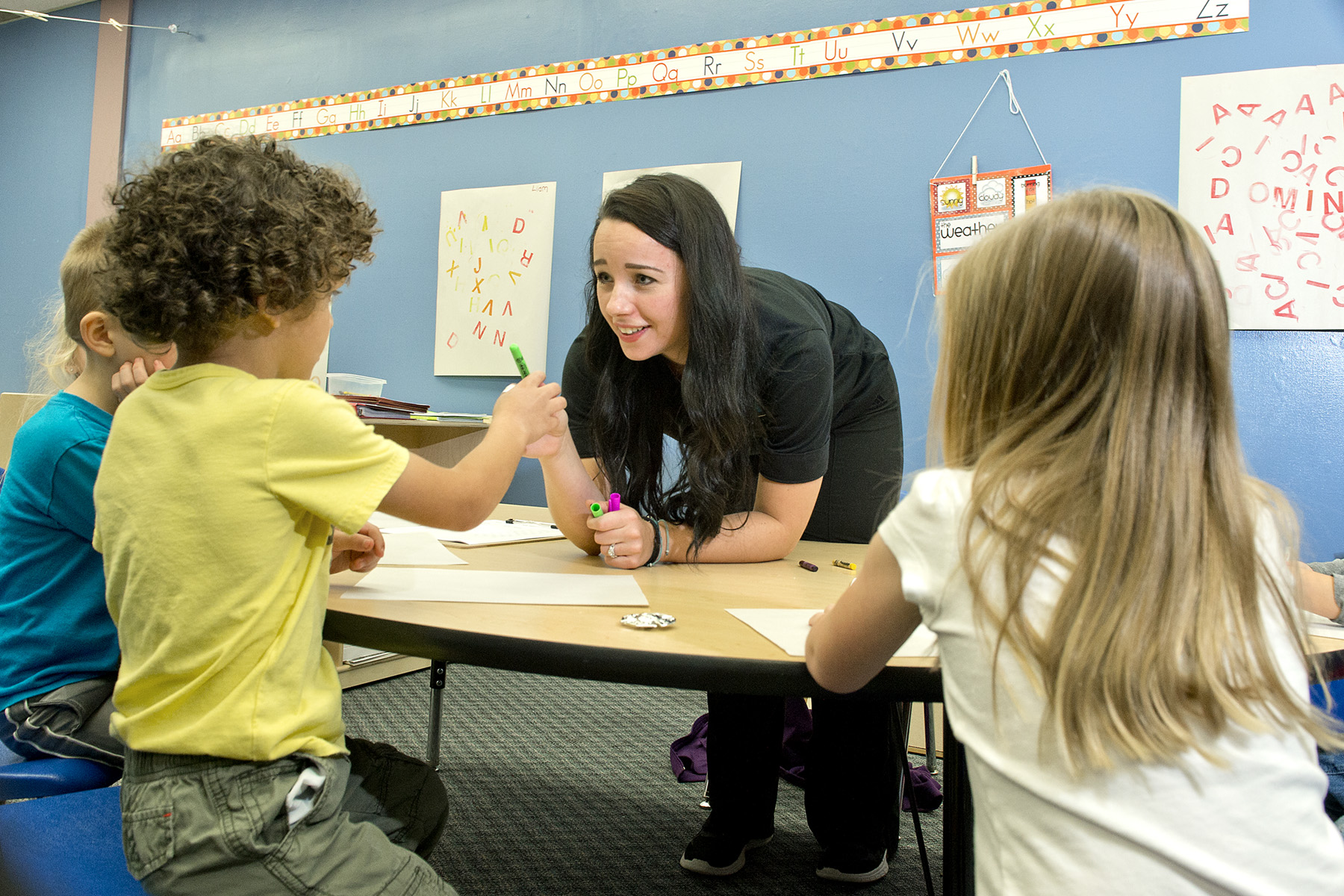 student leaning over to help three small children