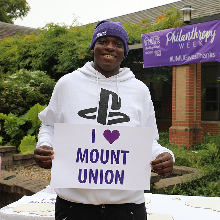 Student during philanthropy week with a sign that says I heart Mount Union