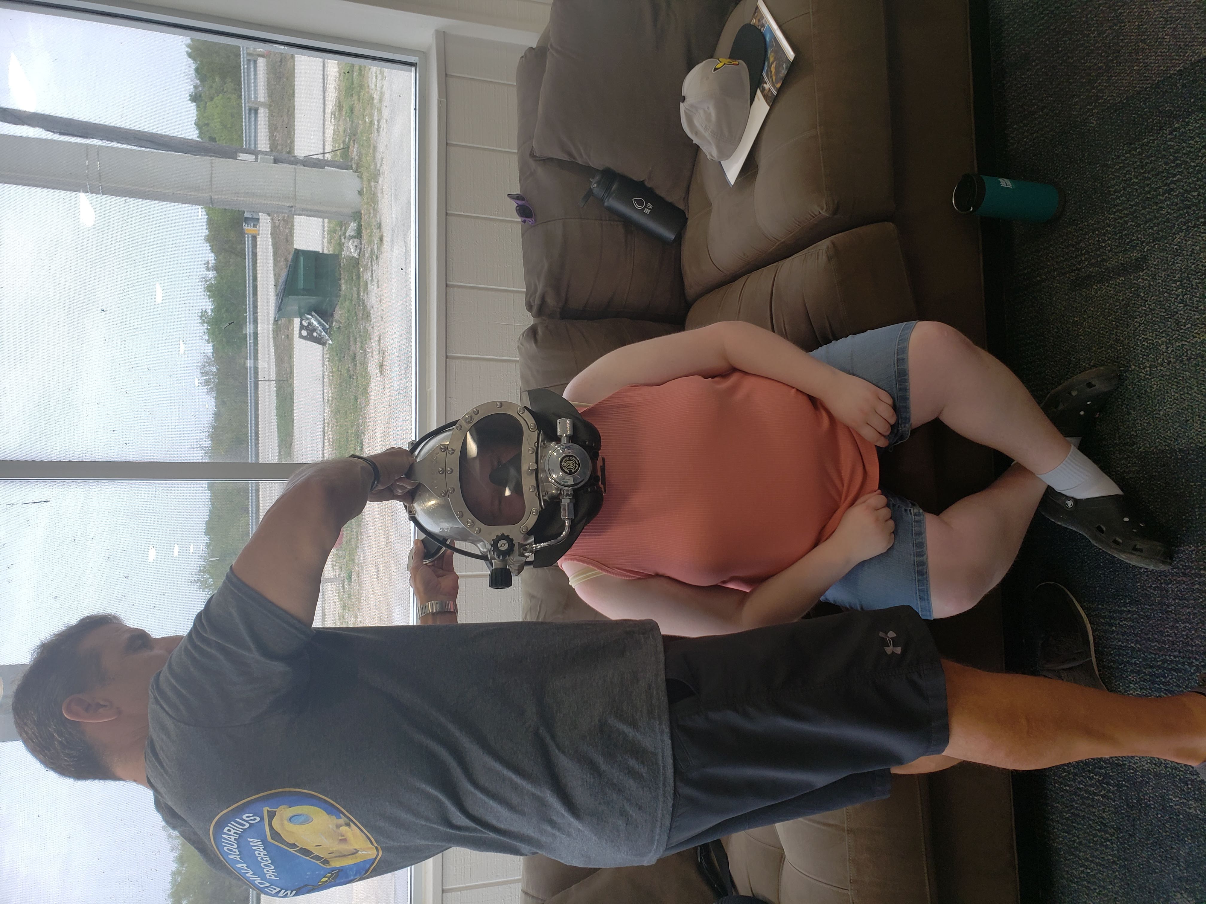 A man assists Emily in putting on a diving helmet
