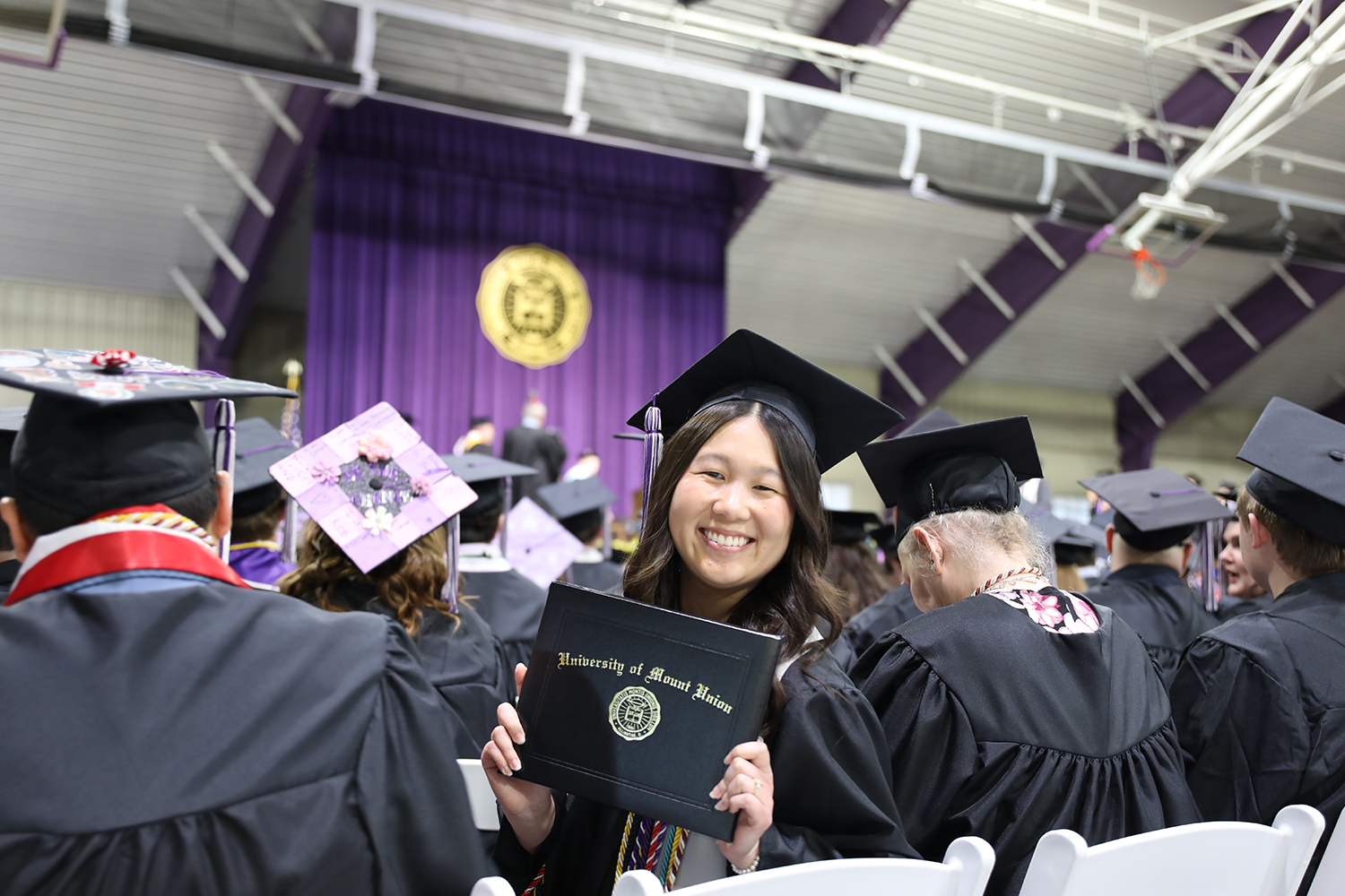 student in graduation crowd holding diploma book