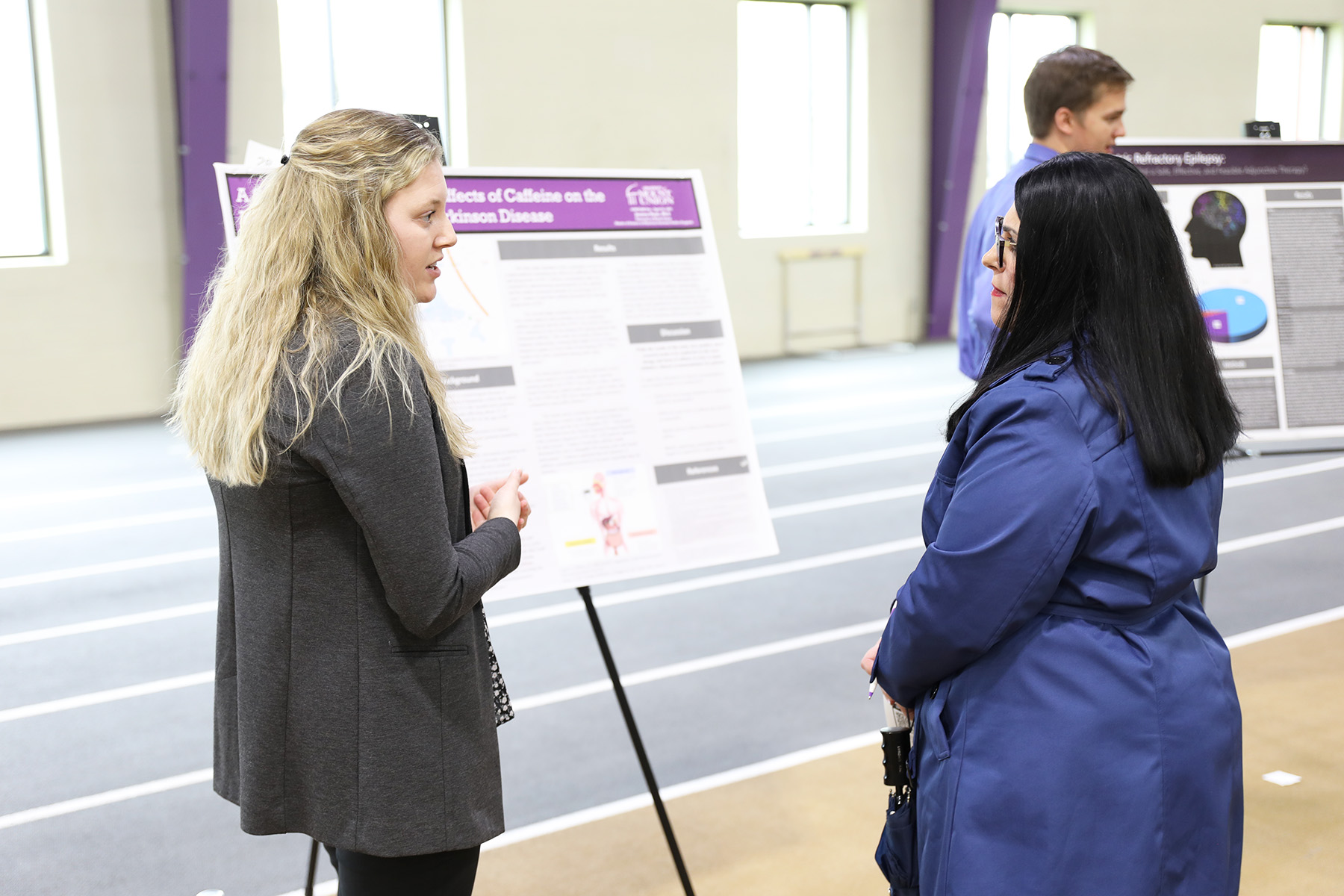 one student talking to woman in front of poster